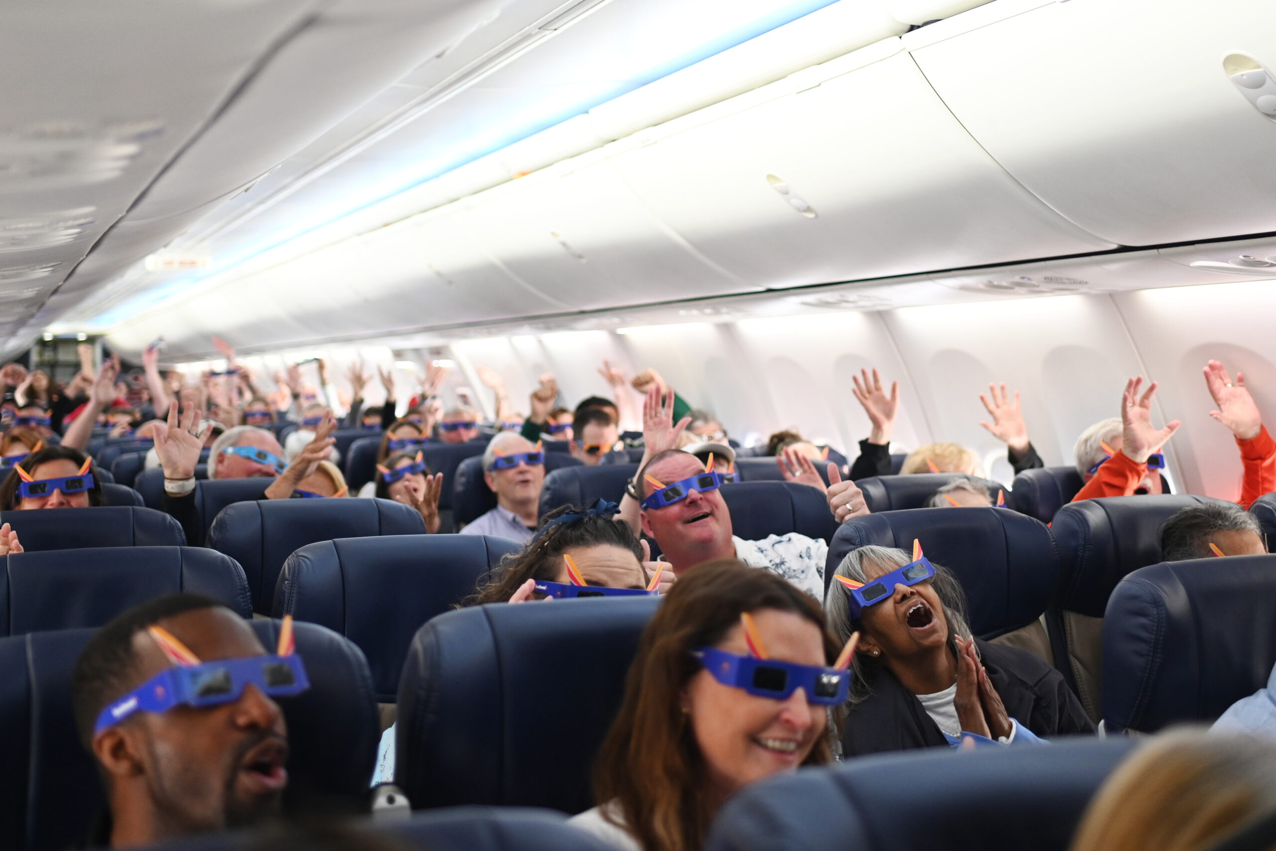 passengers cheer on a plane, wearing eclipse sunglasses