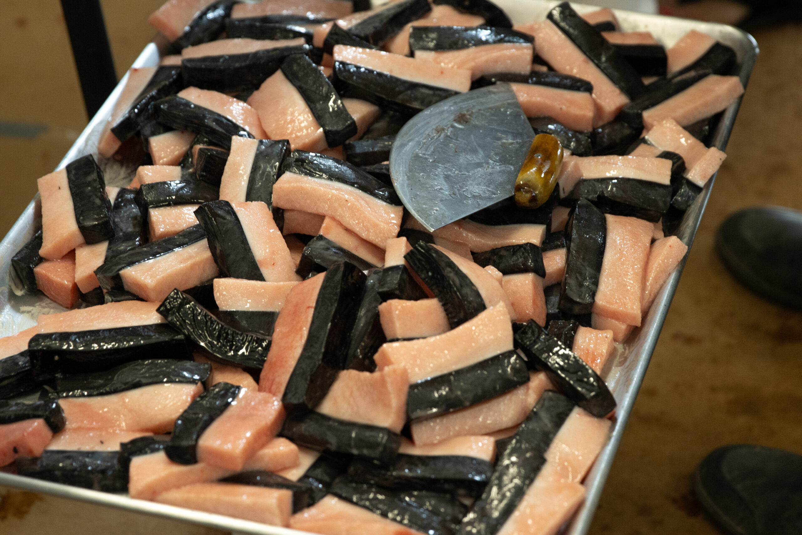 An ulu sits on top of a silver tray stacked with pieces of boiled whale meat.