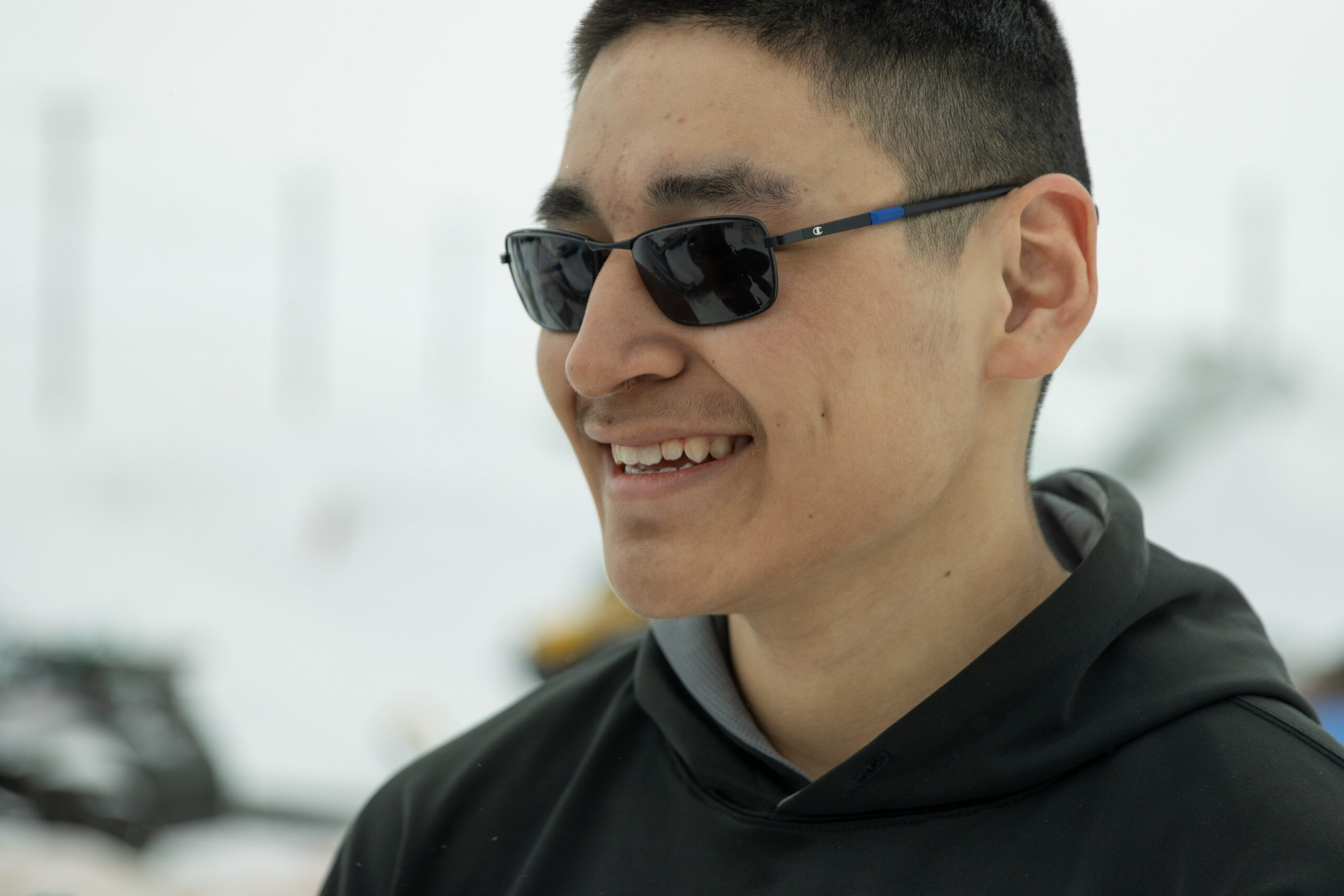 A young man in sunglasses smiles in front of a winter landscape.