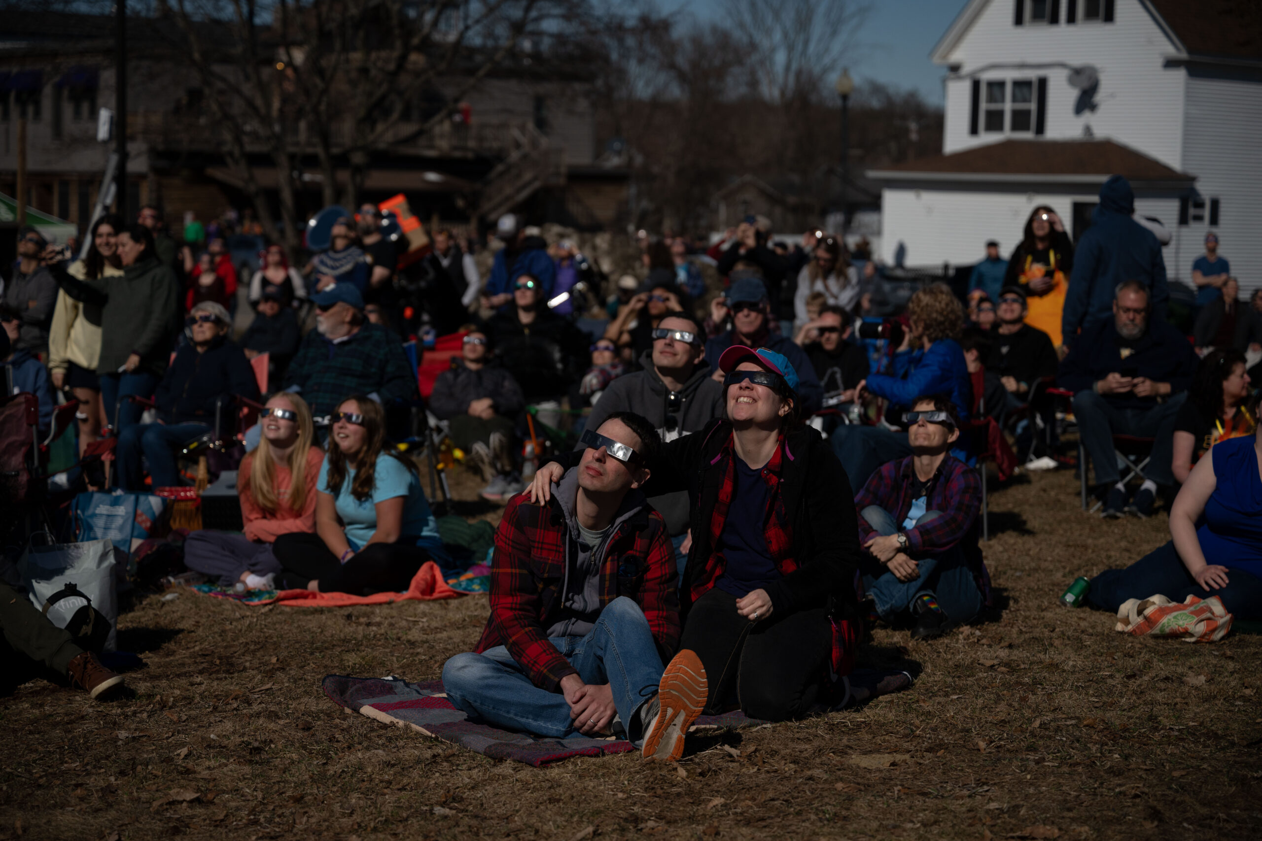 people sit in a field with sunglasses on to view the eclipse