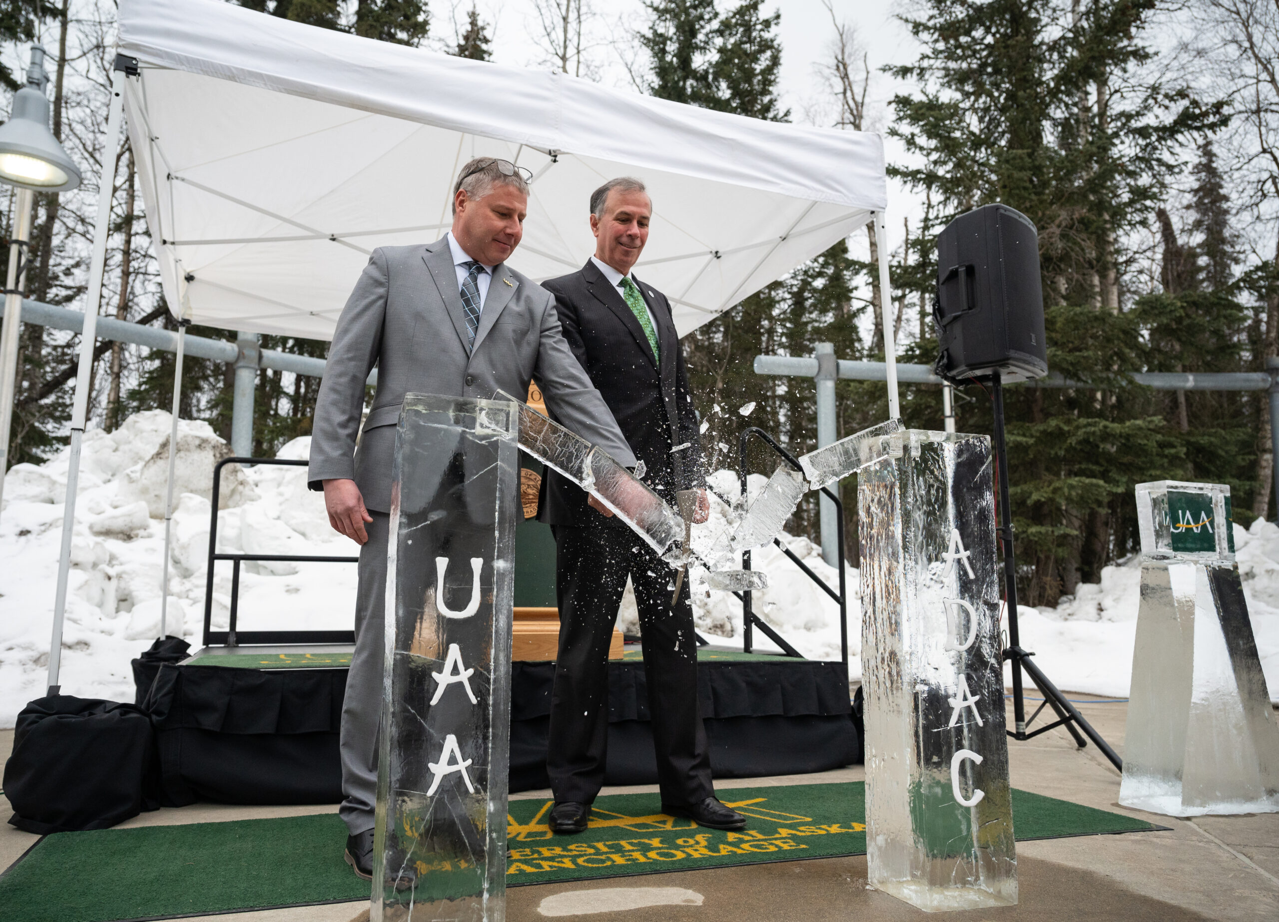 Two men in suits break an ice sculpture with an ice pick