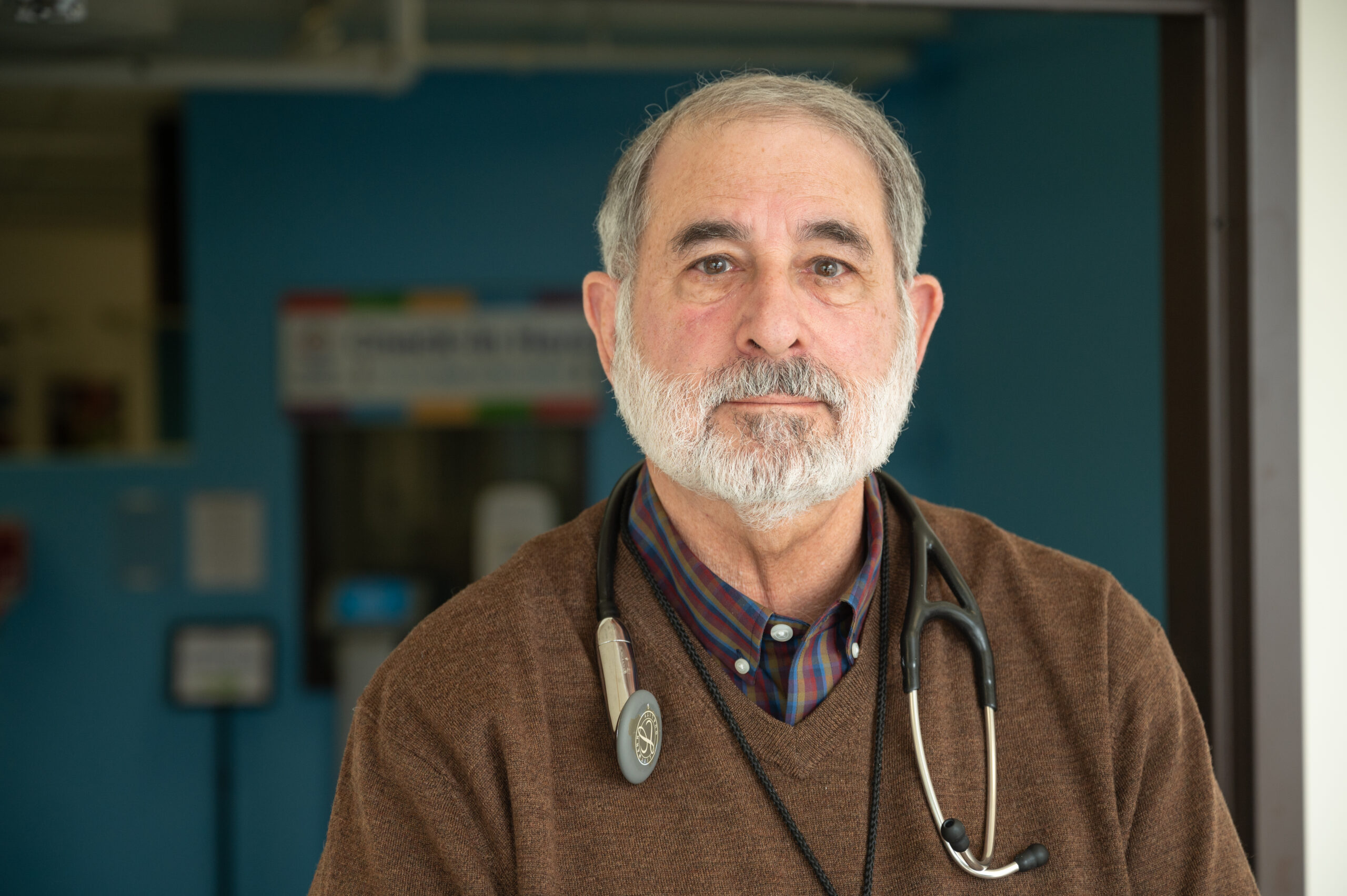 A doctor with a brown sweater stands in front of an emergency room