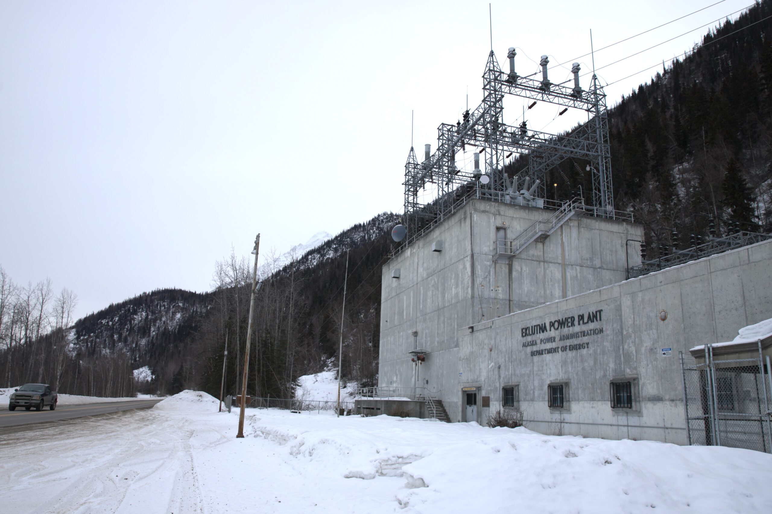 A gray concrete building labeled Eklutna Power Plant along a snowy road