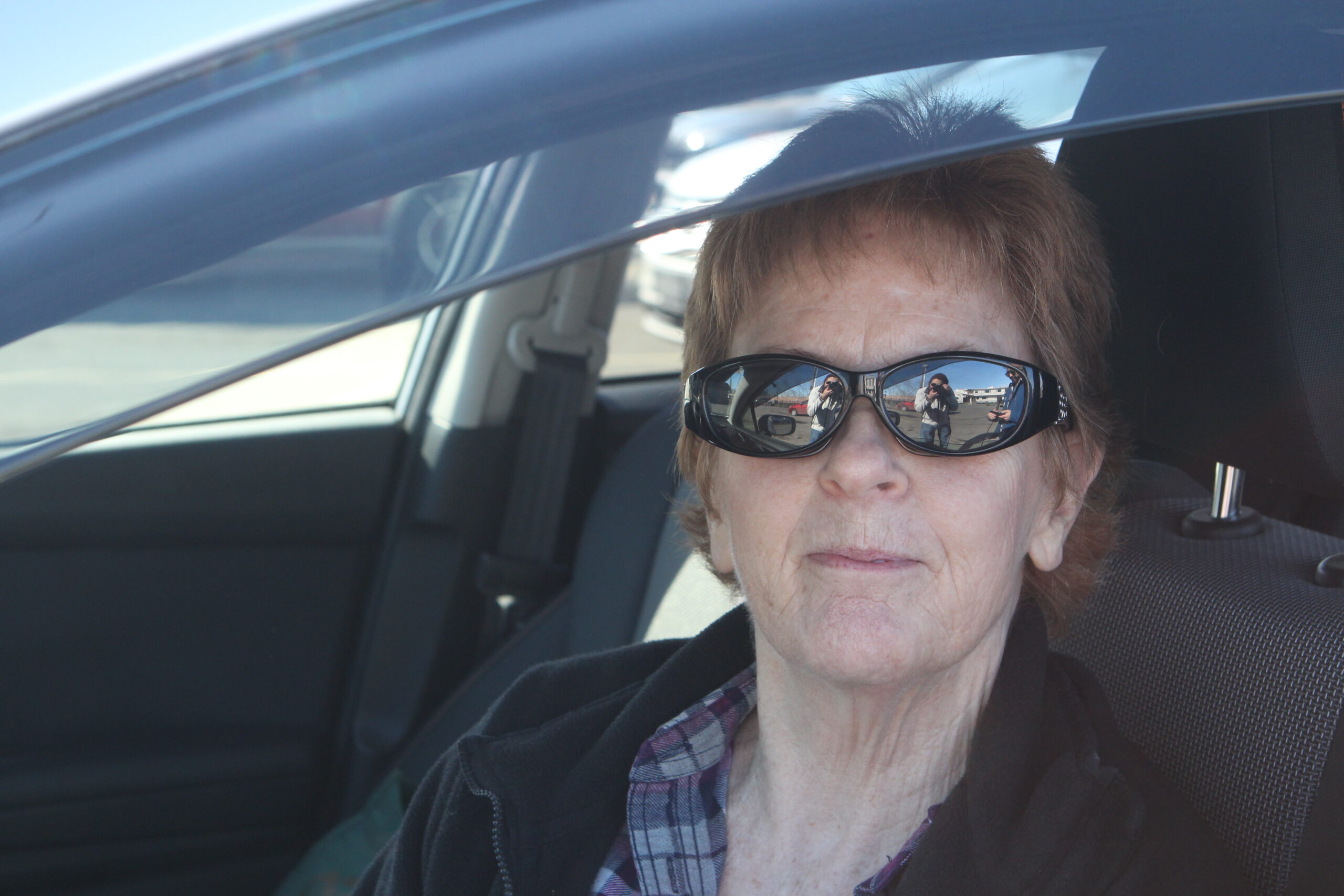 a woman in sunglasses sits in her car