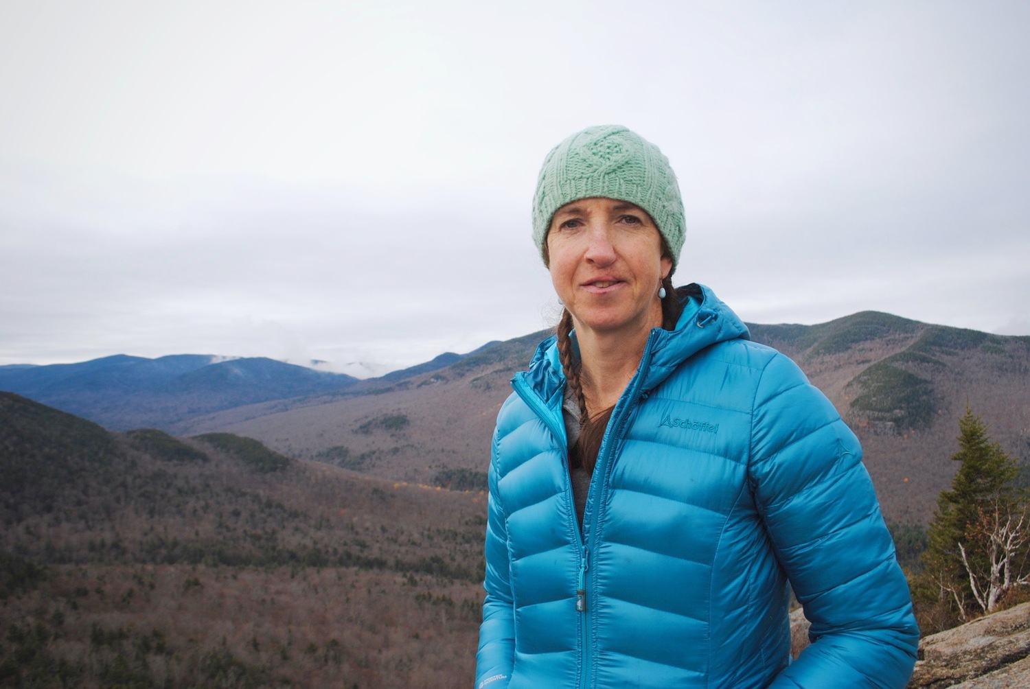 a portrait of a woman in a blue jacket in the mountains