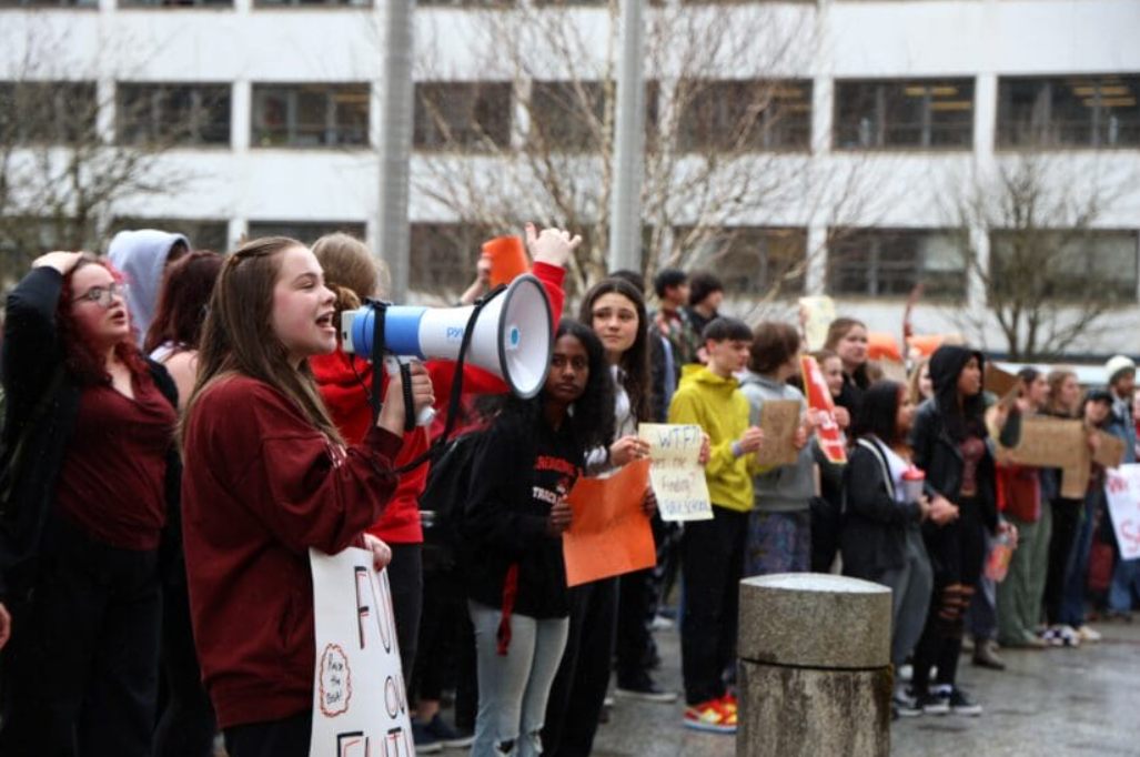 A high school student holds a megaphone while protesting in front of the Alaska Capitol.
