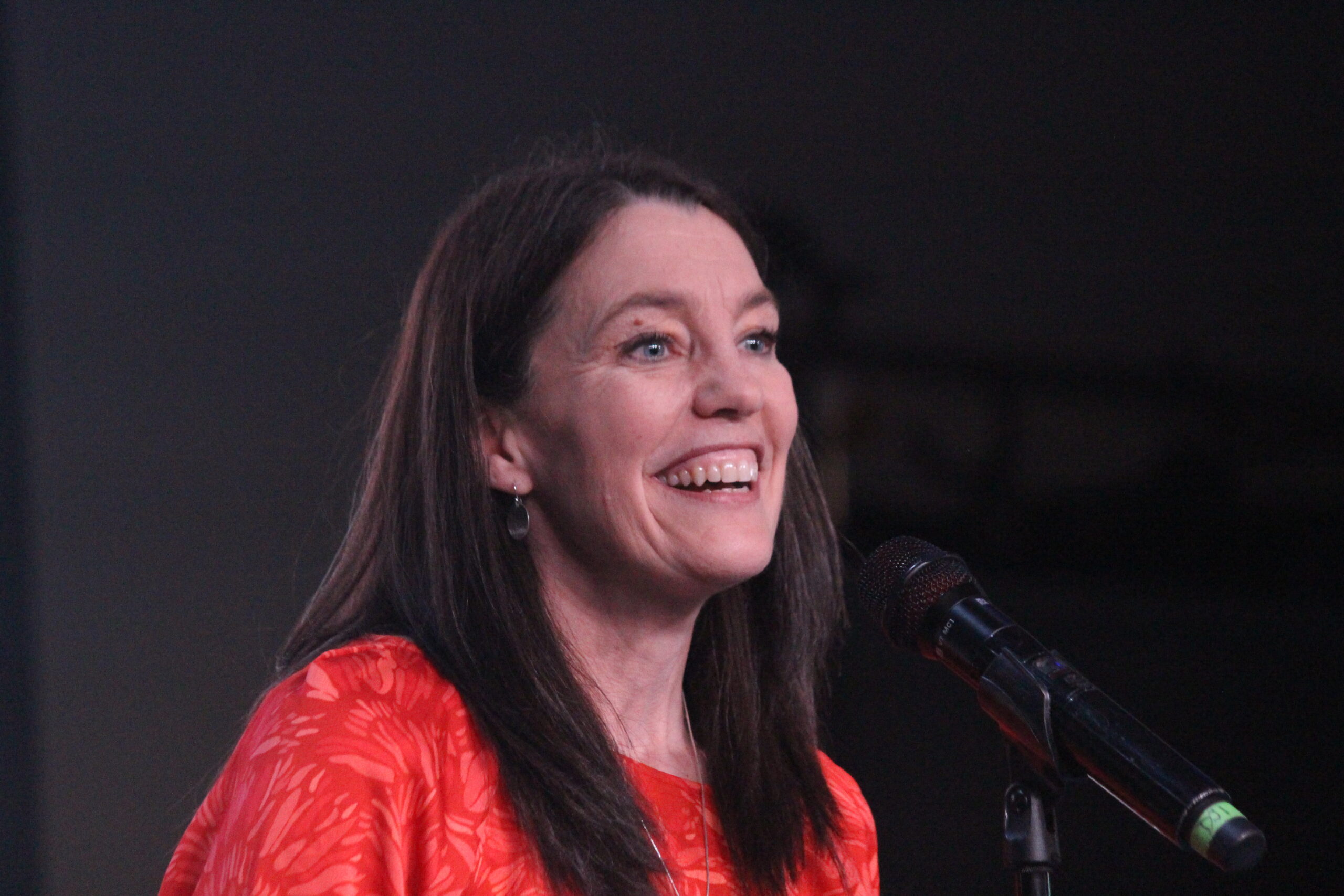 a woman in red speaks at a microphone