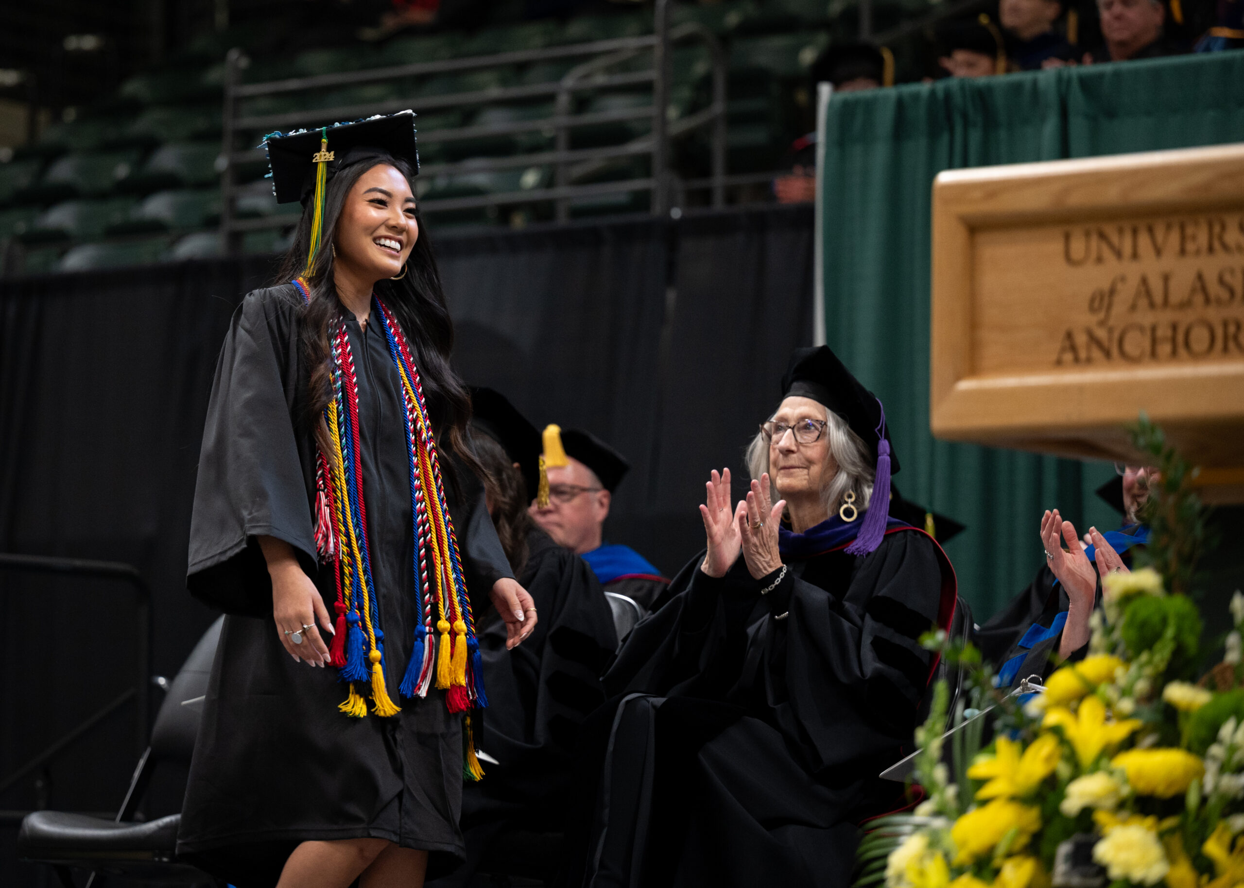 A woman in a black graduation gown walks up to a podium.