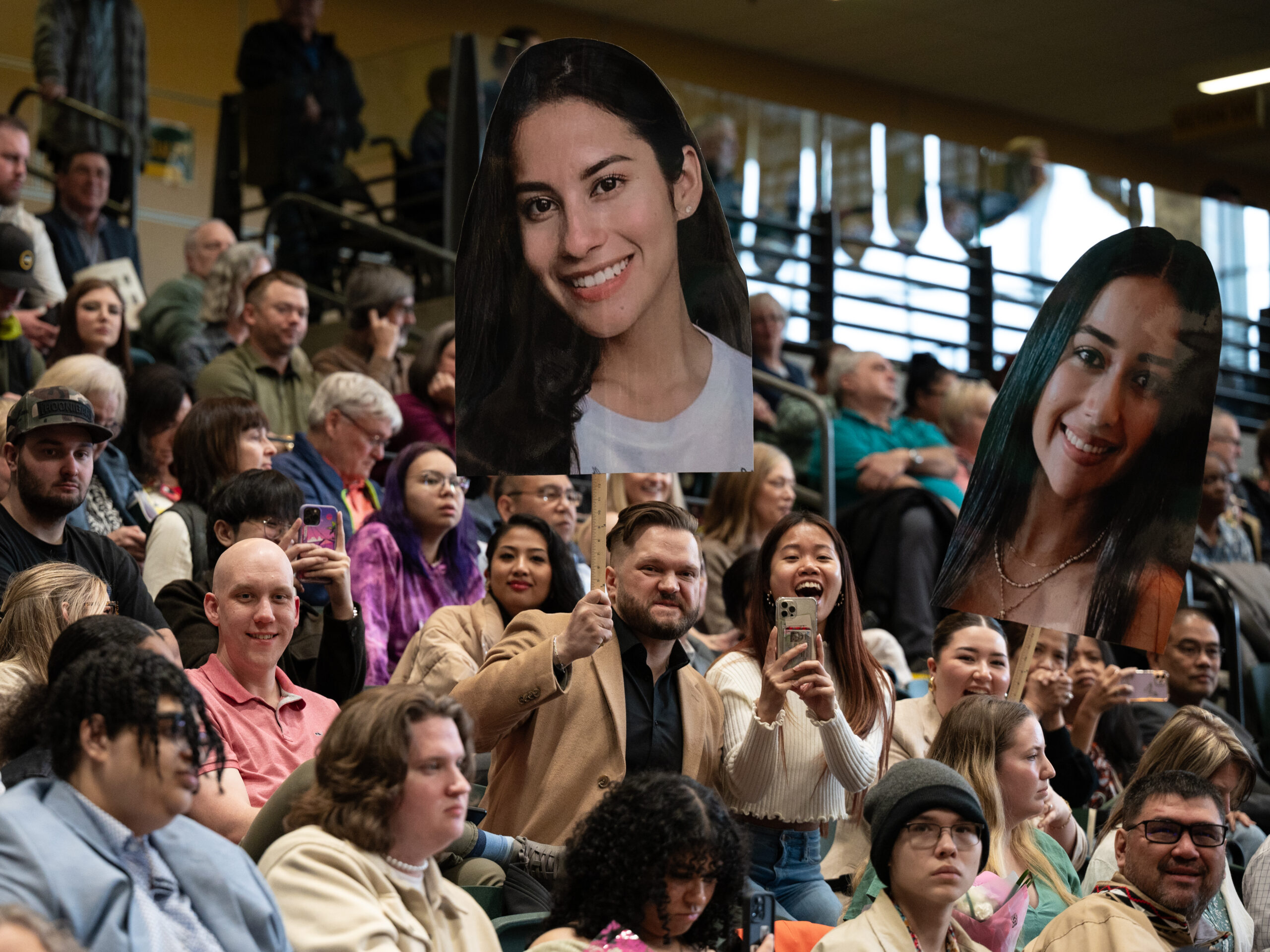 people hold cardboard cutouts of a person's head in the air at a graduation, while cheering