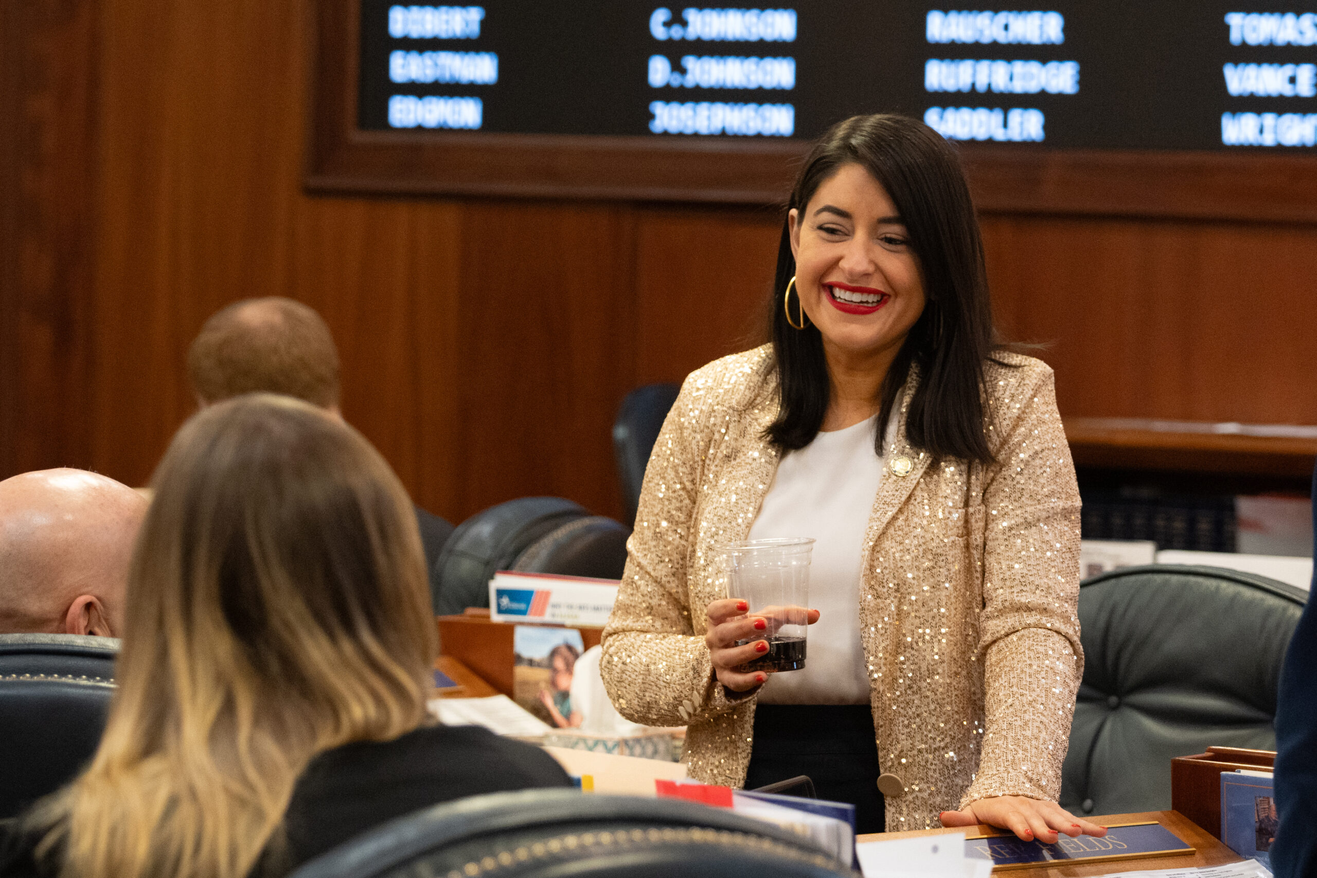 A woman smiles and holds a plastic cup in the state legislature.