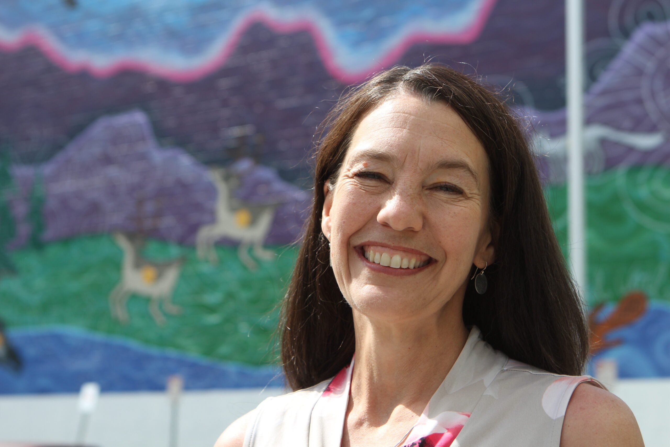 a woman smiles in front of a mural