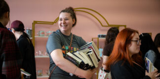 A woman with a bunch of books waits in line.