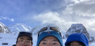 A selfie of three men wearing jackets and hats, surrounded by snow and mountains.