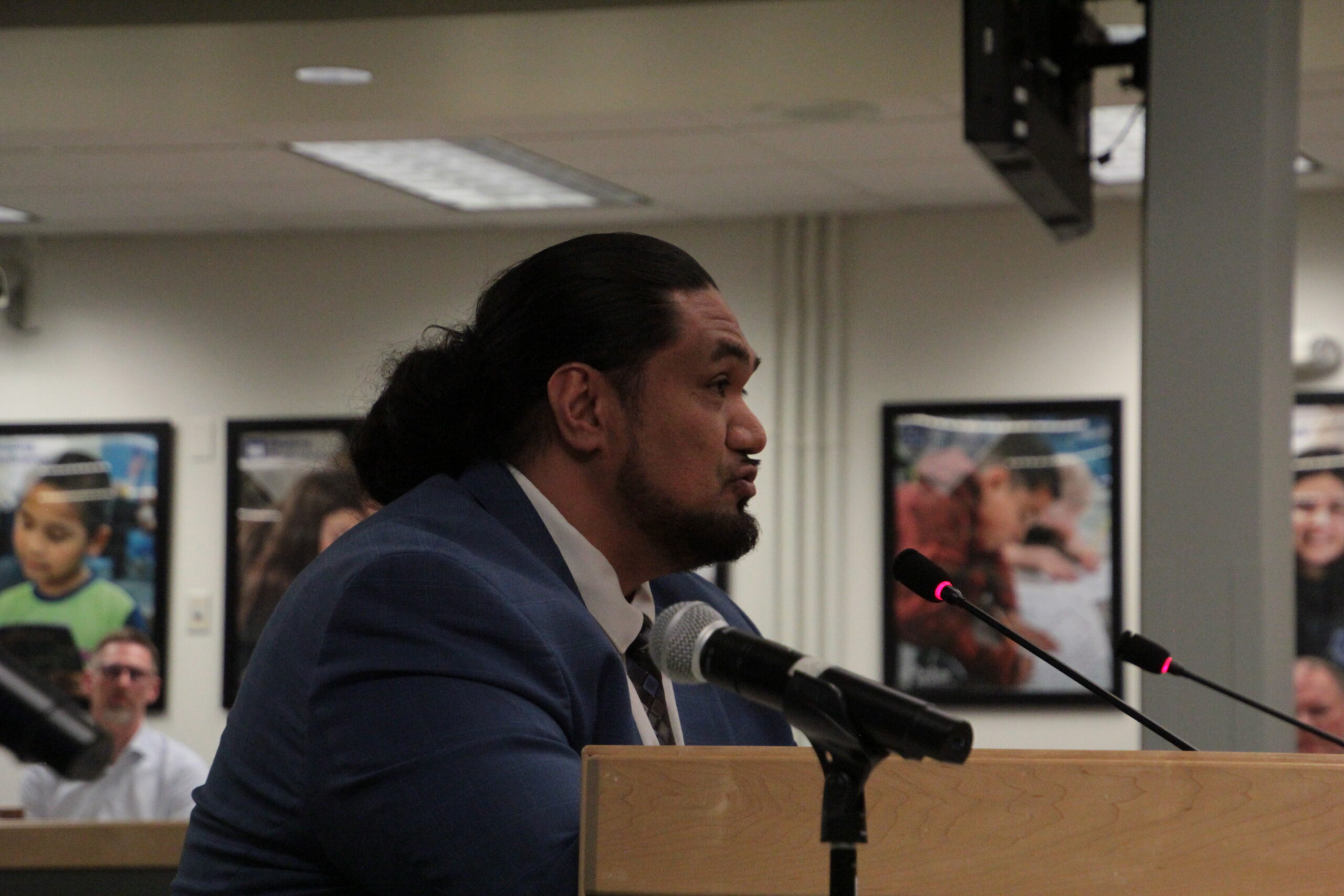 A man in a blue suit jacket speaks at a school board meeting