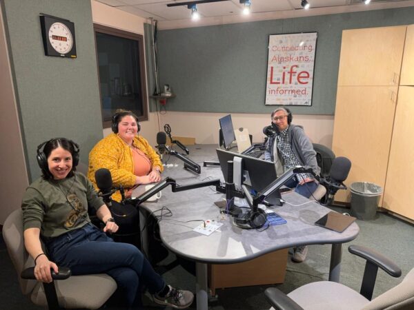 Three people pose in a radio studio. 