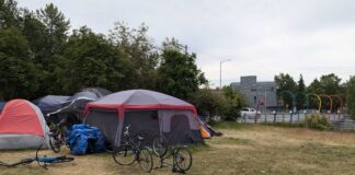 bicycles and tents stand in a field near a road overpass