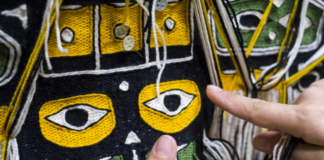 A woman points to the color of yarn in a Chilkat Robe.