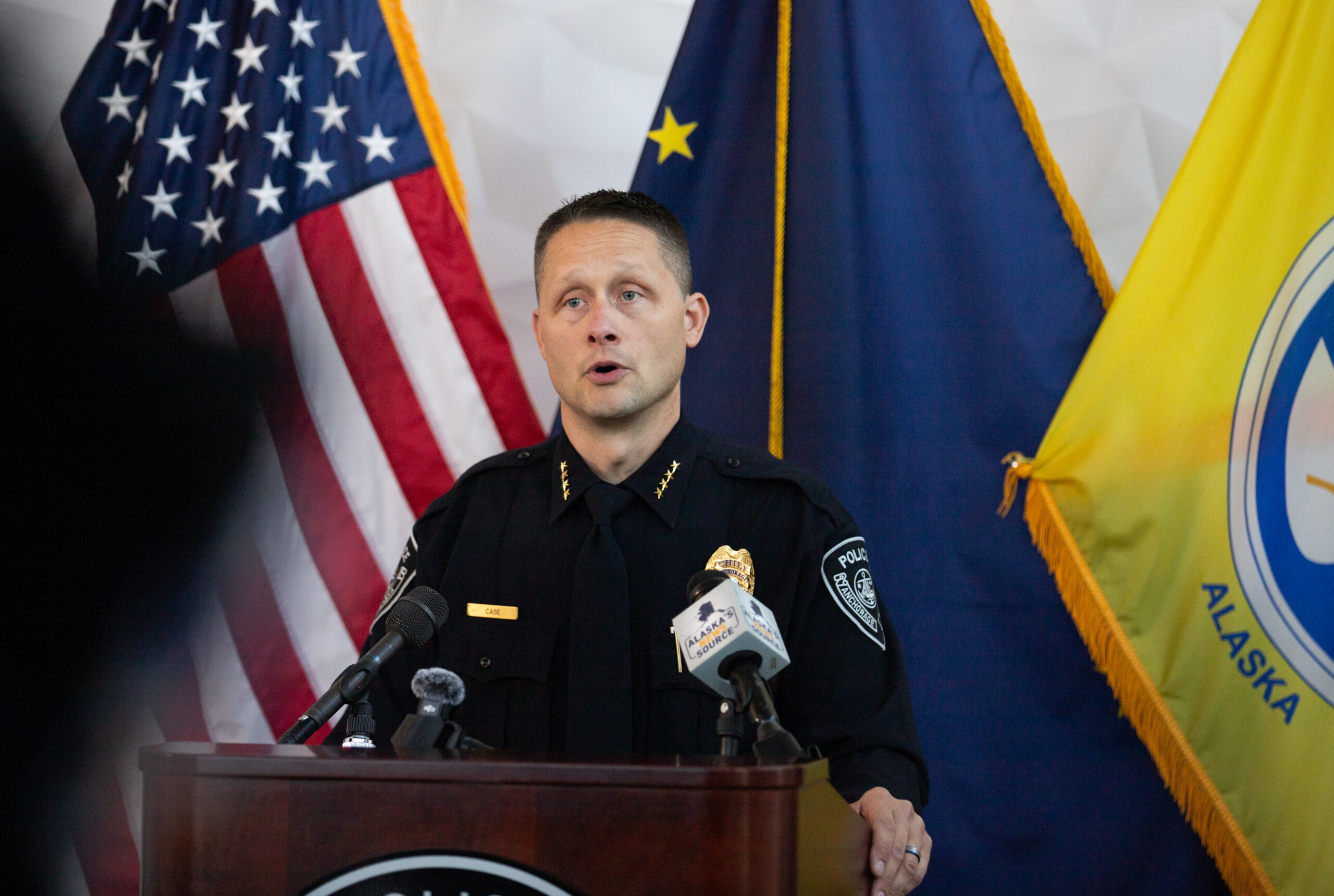 A police man speaking behind a podium with flags in the back