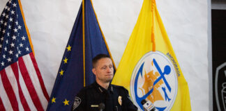 A police man speaking behind a podium with flags in the back