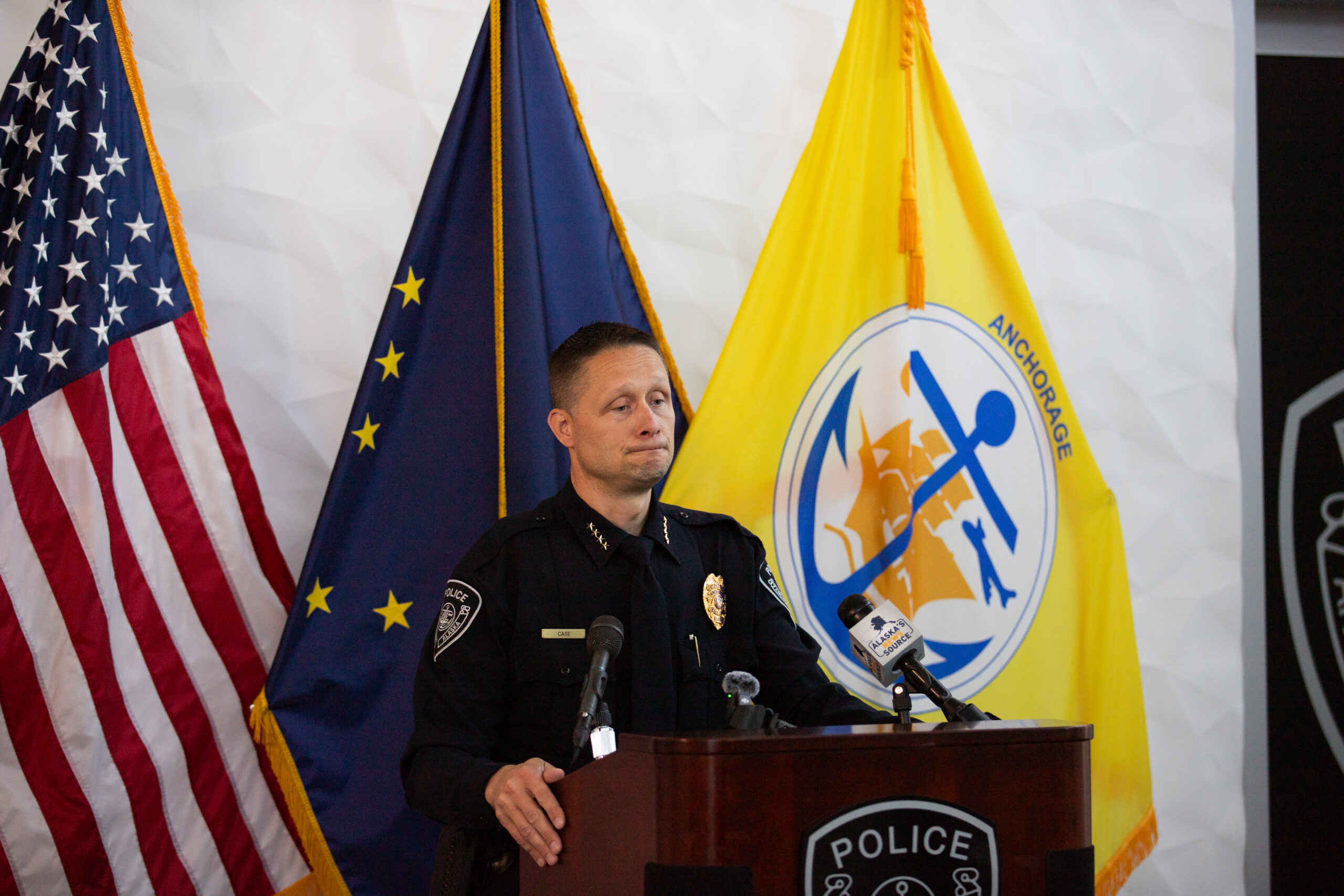 A police man speaking behind a podium with flags in the back
