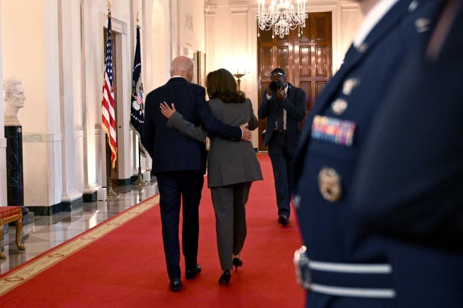 two peole walk down a hallway in the white house, with their arms around each other's backs