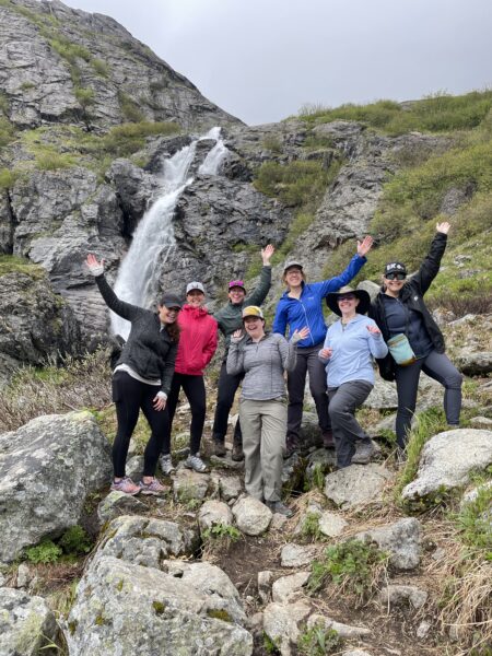 A group of hikers pose in front of a waterfall. 