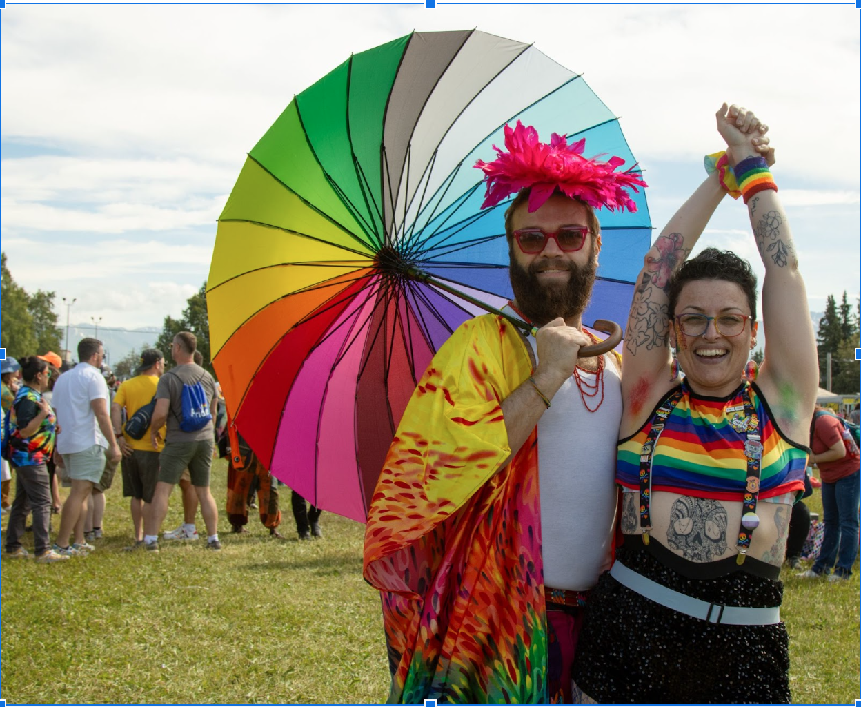 Two adults wearing rainbow clothing and 1 holding an umbrella grin successful a photo.