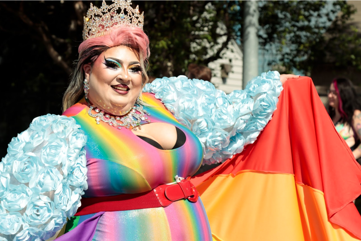 Drag queen wearing crown and gown holds pride flag.