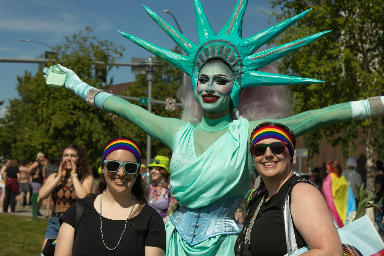 Drag queen Lamina poses with two women in rainbow headbands dressed as the statue of liberty.