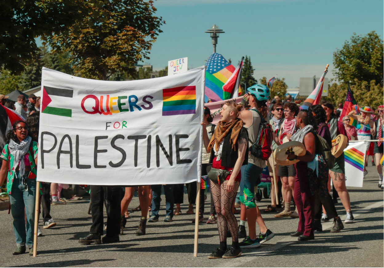 Organizers from the Queers for Palestine group hold a banner with the Palestine flag, the rainbow flag and the words "queers for Palestine."