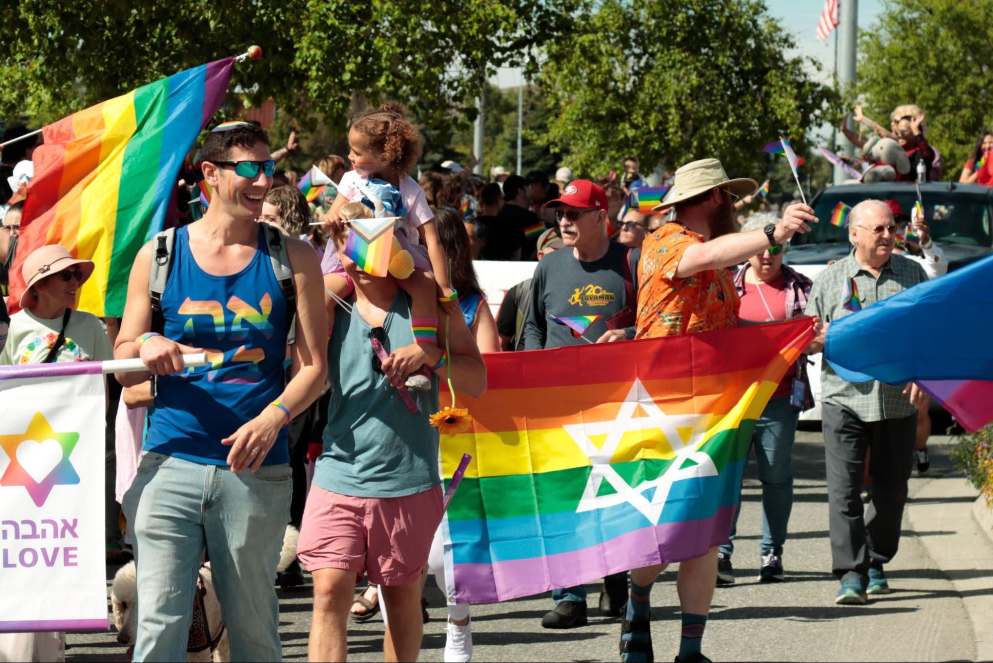 people walk in a parade with rainbow flags, waving