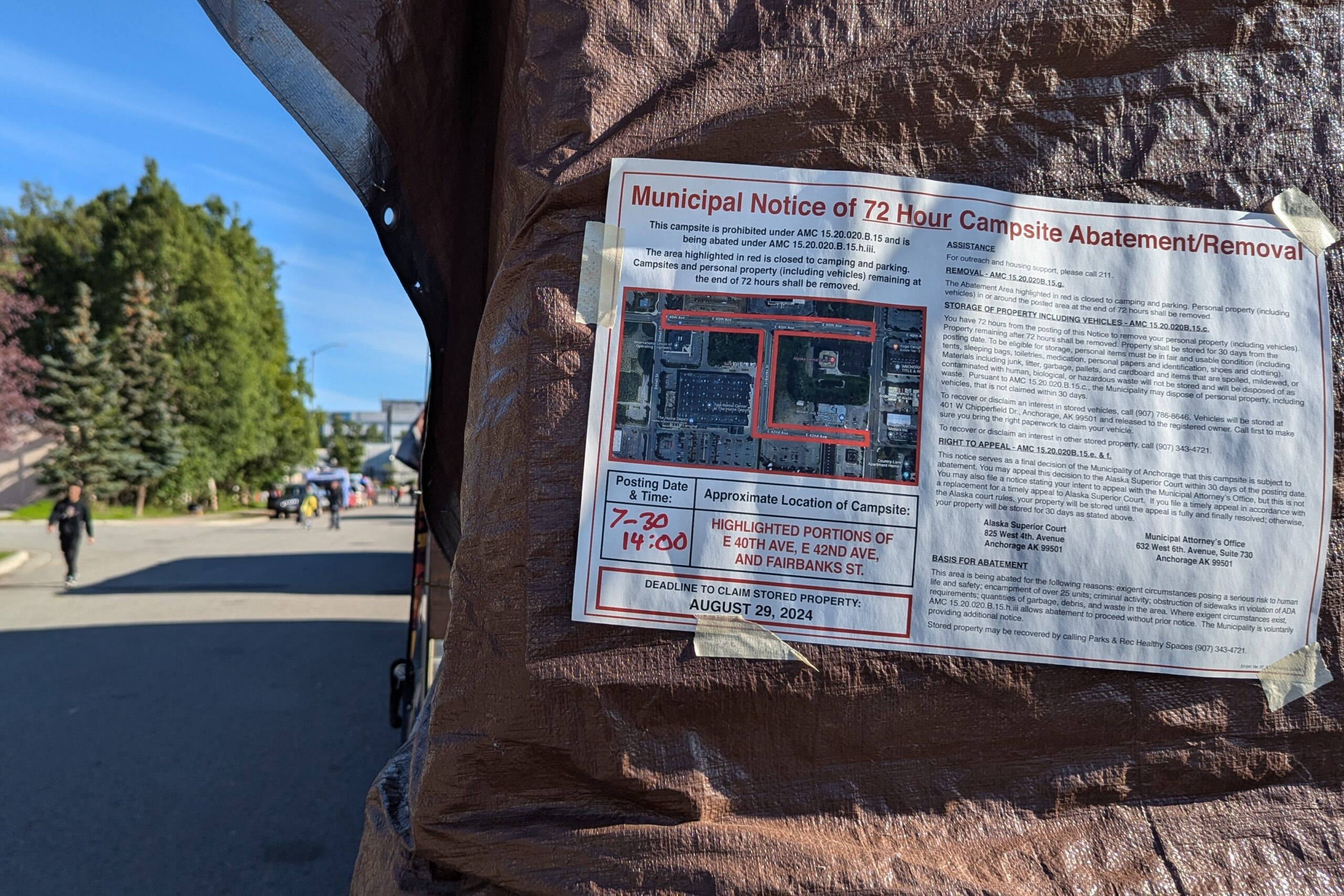 An abatement notice is taped to a brown tarp on a street with many makeshift shelters