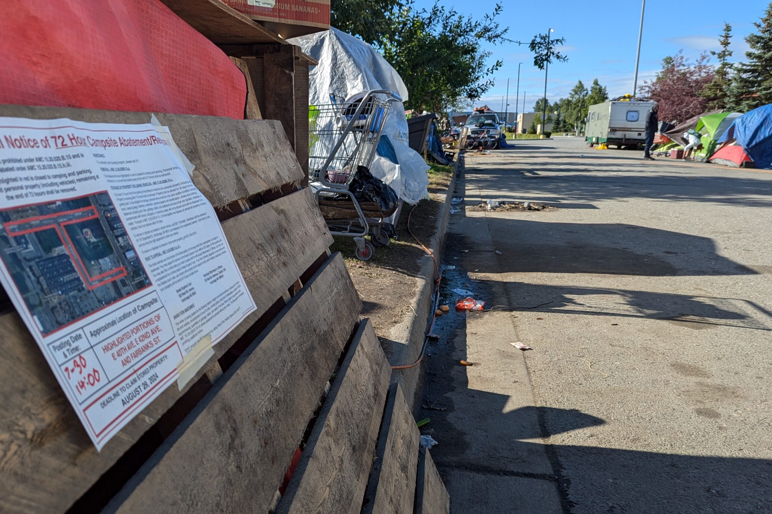 An abatement notice is taped to a wooden pallet leaning against a makeshift shelter on a street with many makeshift shelters