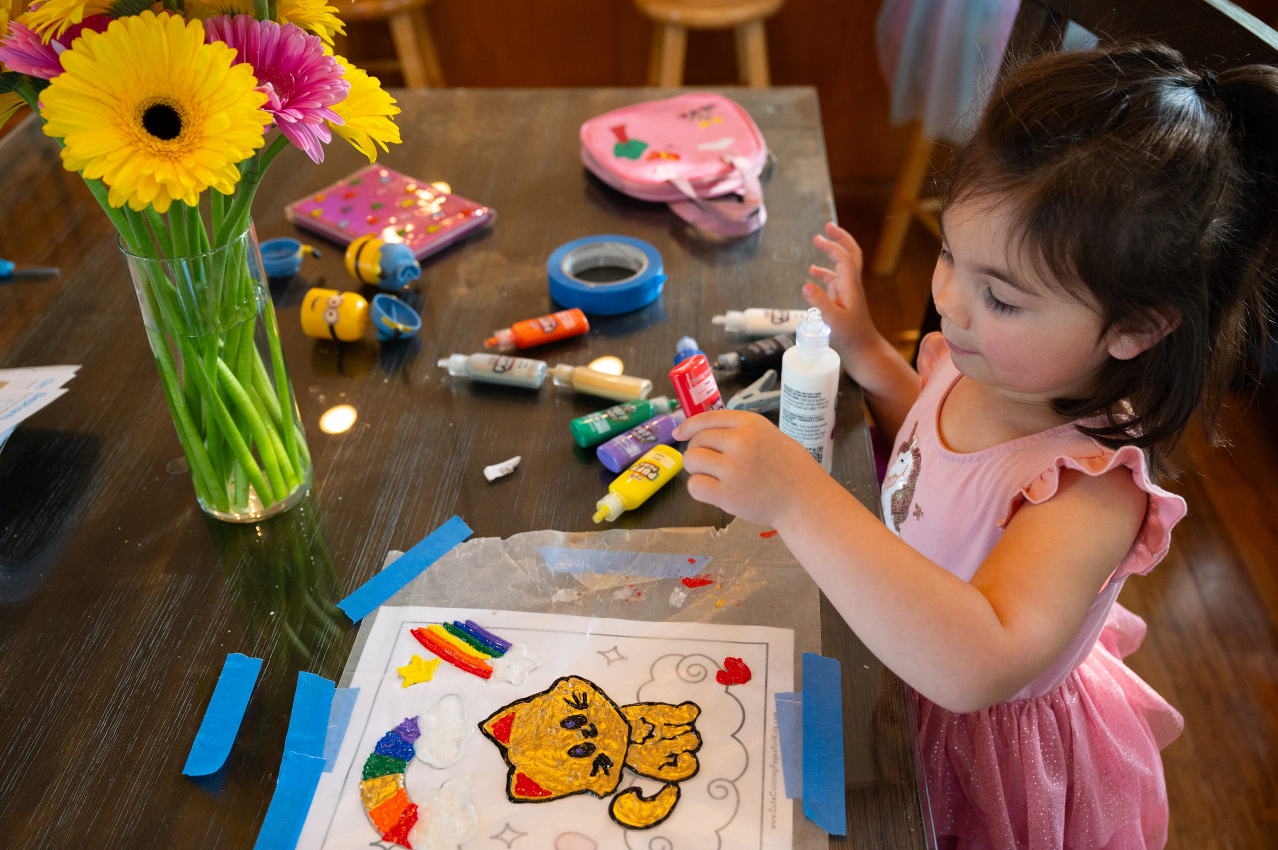 A girl sits at the dining room table and paints a picture.