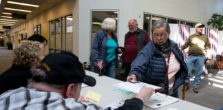 A woman wearing a puffy vest receives a voter ballot.