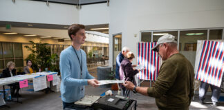 A man in a blue shirt takes a ballot from a voter.