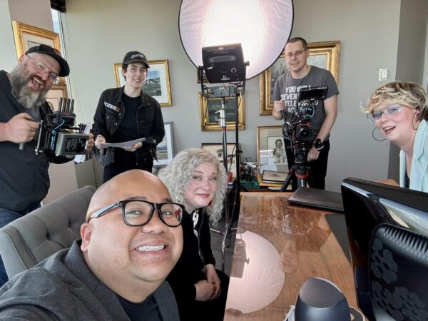 A group of people pose around a desk during filming of a show. 