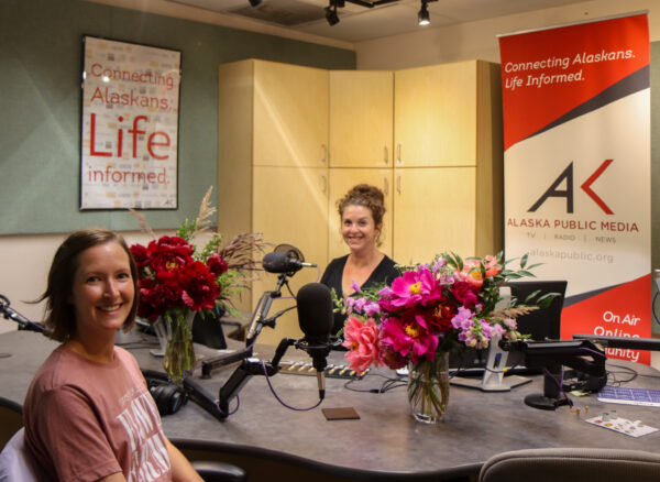 Two women sit in a radio studio with bouquets of flowers.