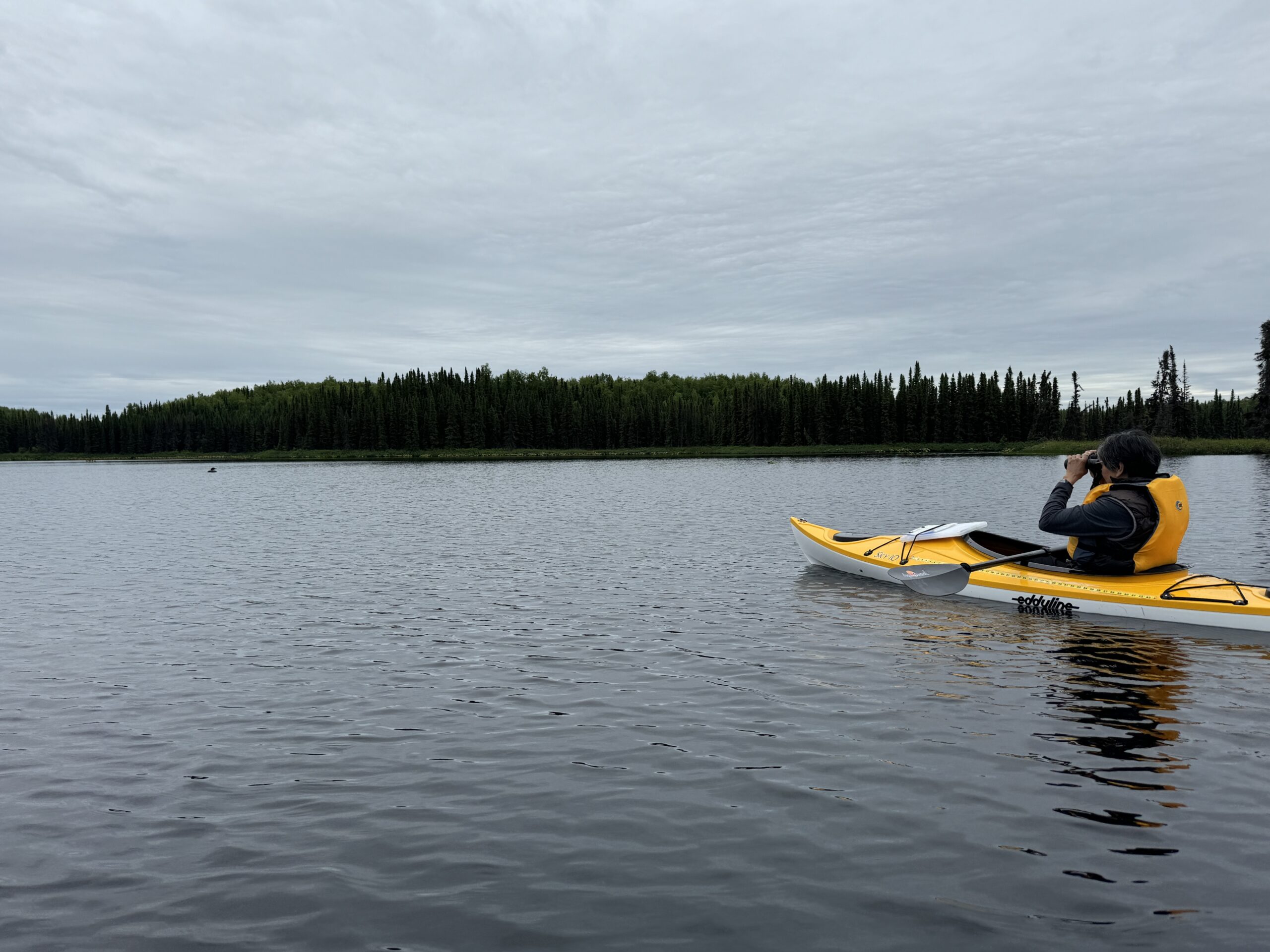 A female holds binoculars to her eyes arsenic she sits successful a kayak connected a lake. 