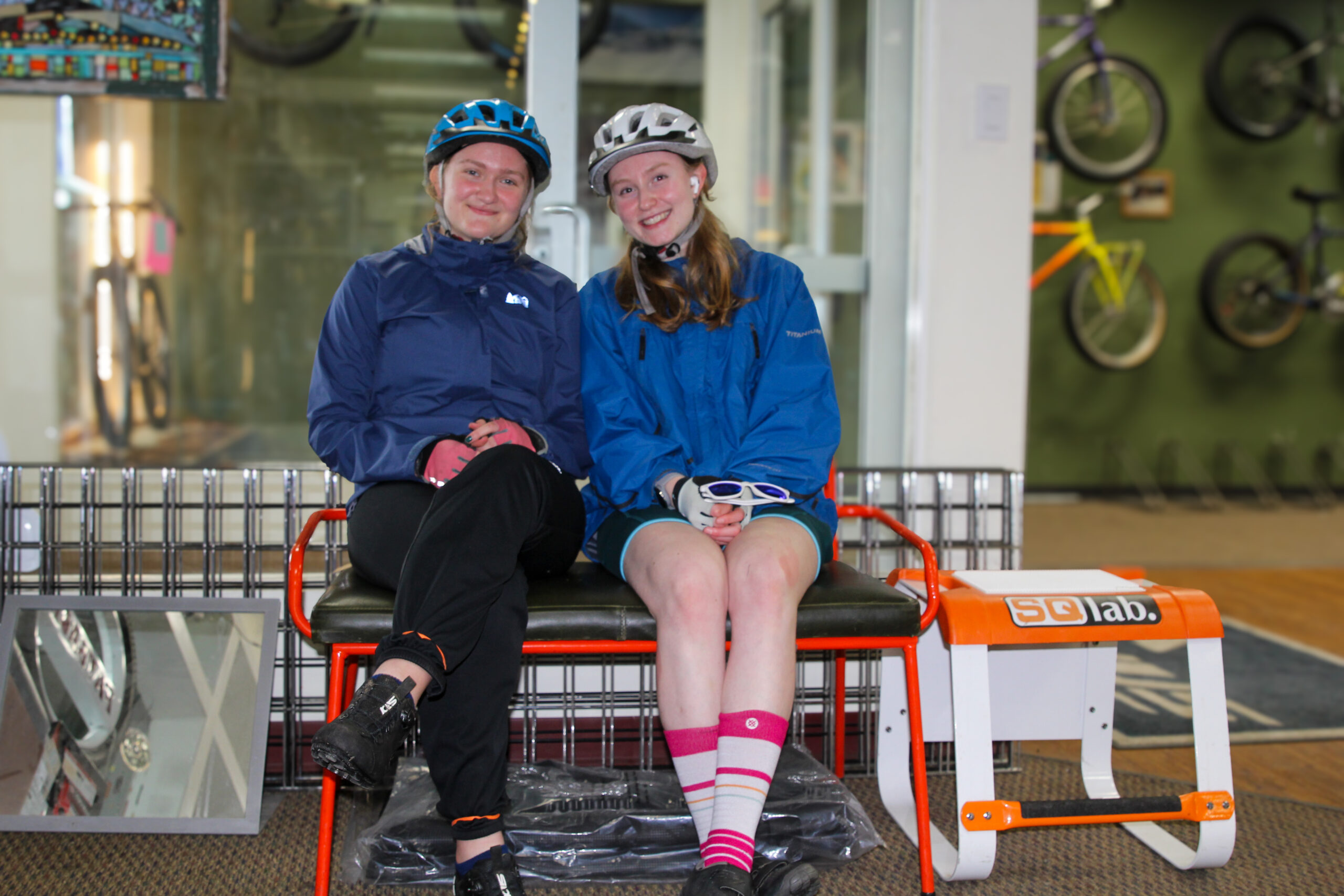 two young women successful bluish rainfall jackets beryllium connected a chair wrong a bicycle shop smiling and wearing helmets