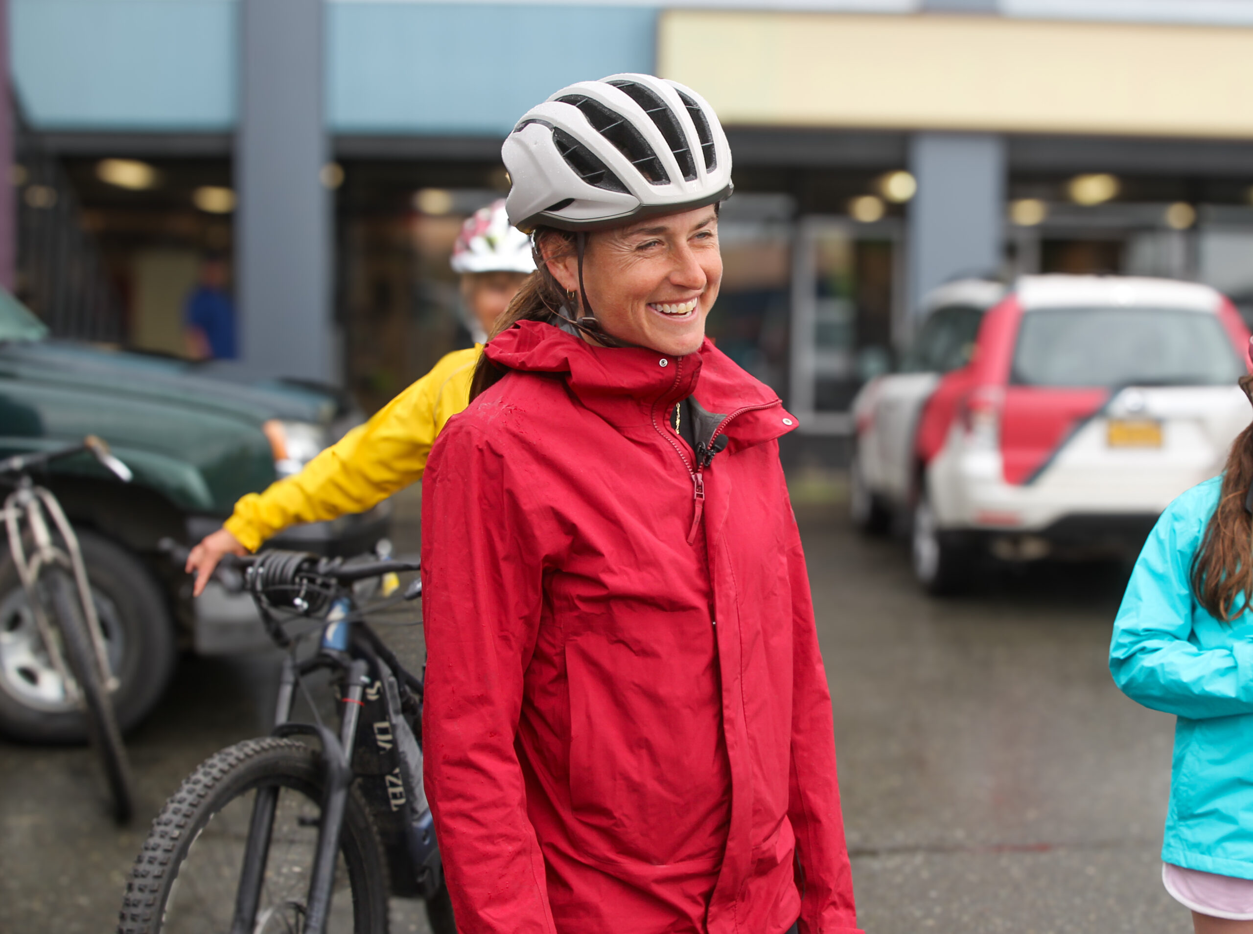 a female successful a reddish rainfall overgarment and achromatic helmet smiles big. location is different personification down her connected a bike