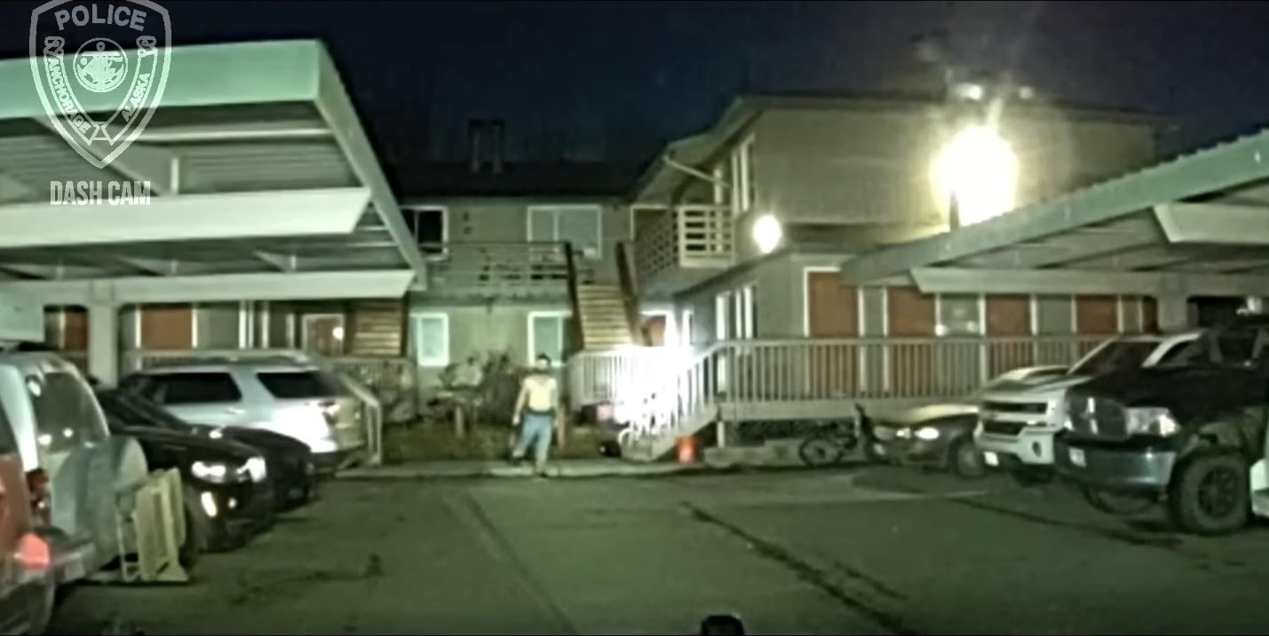 a grainy video still of a shirtless man holding a shotgun stepping off a curb