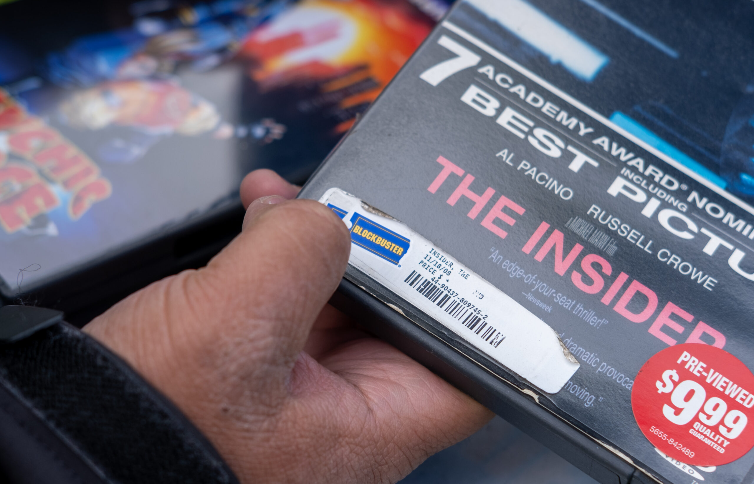 a close up of a man's hand holding a DVD case. the case says "the insider, an edge of your seat thriller! pre-viewed $9.99 quality guaranteed" 