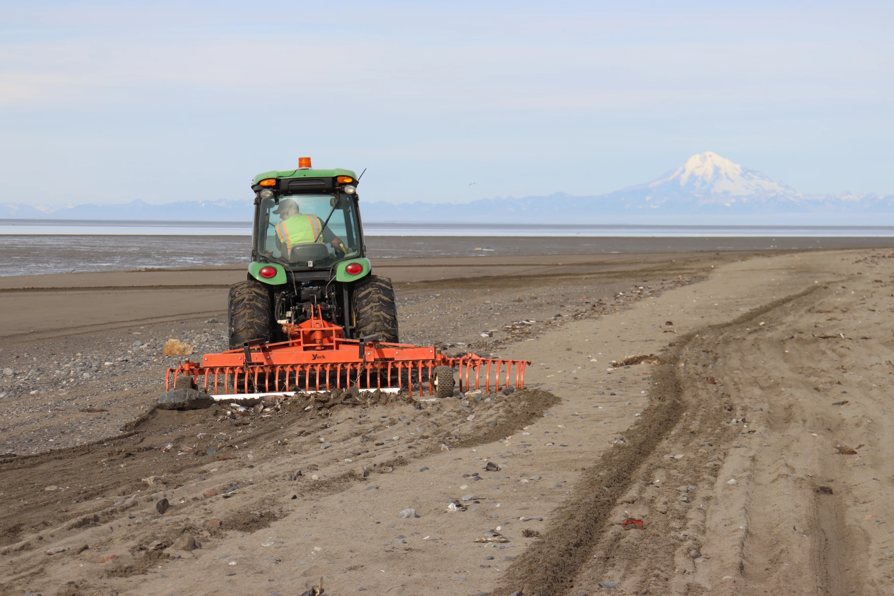 A man drives a tractor dragging a rake on the beach in Kenai