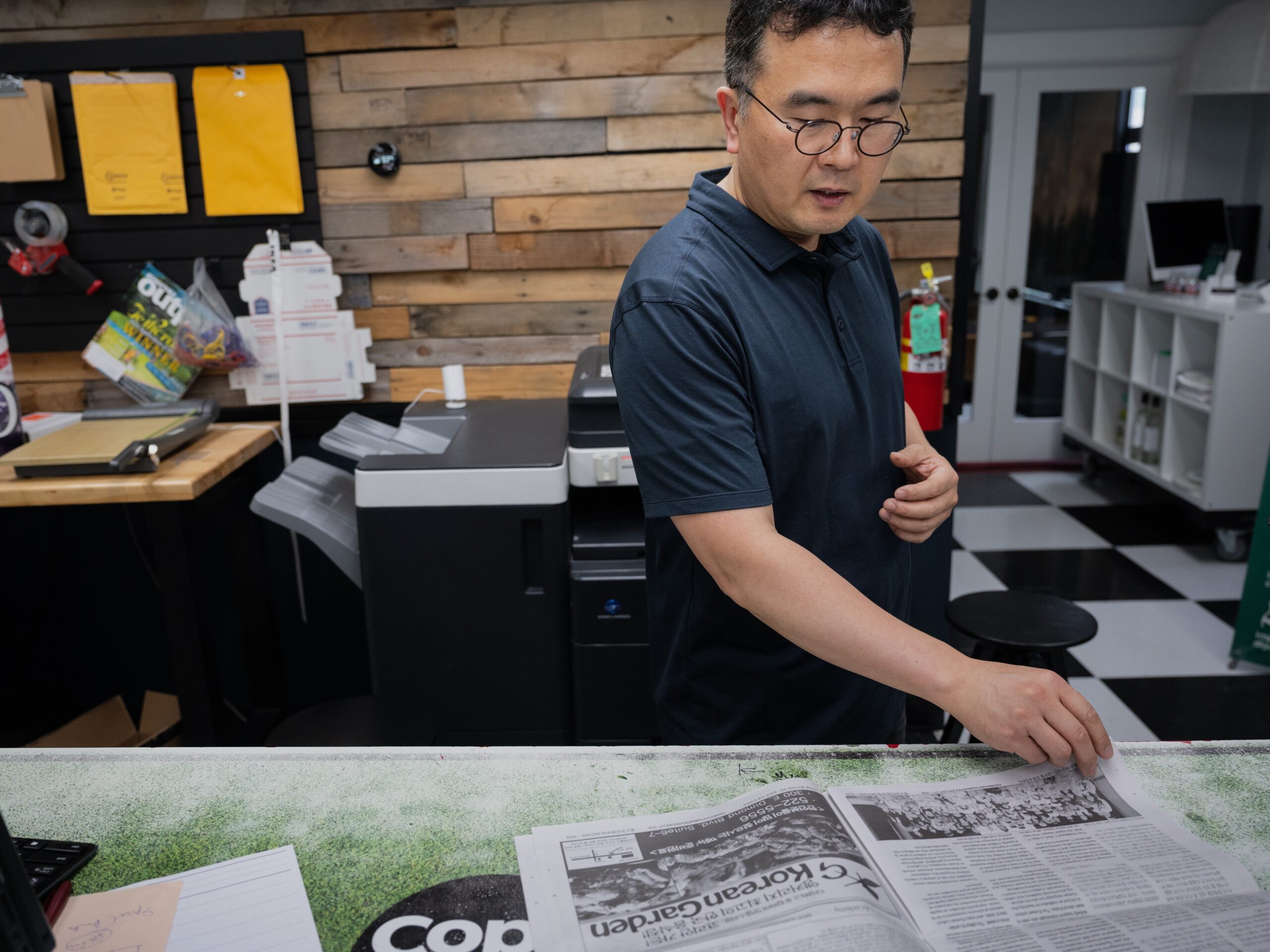 a Korean man behind a counter flips through a newspaper