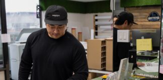 a Korean man in front of a counter flips through a newspaper