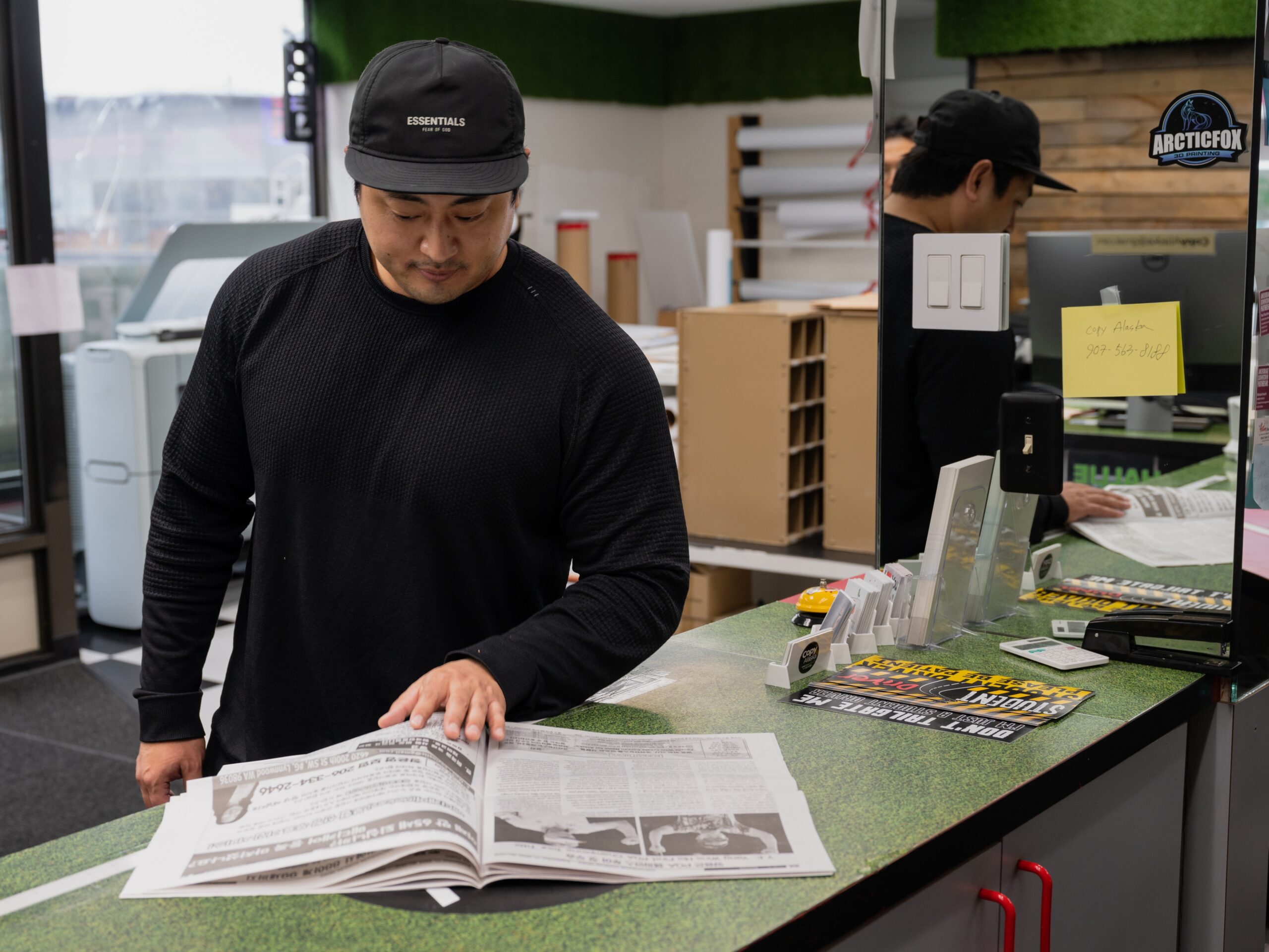 a Korean man in front of a counter flips through a newspaper