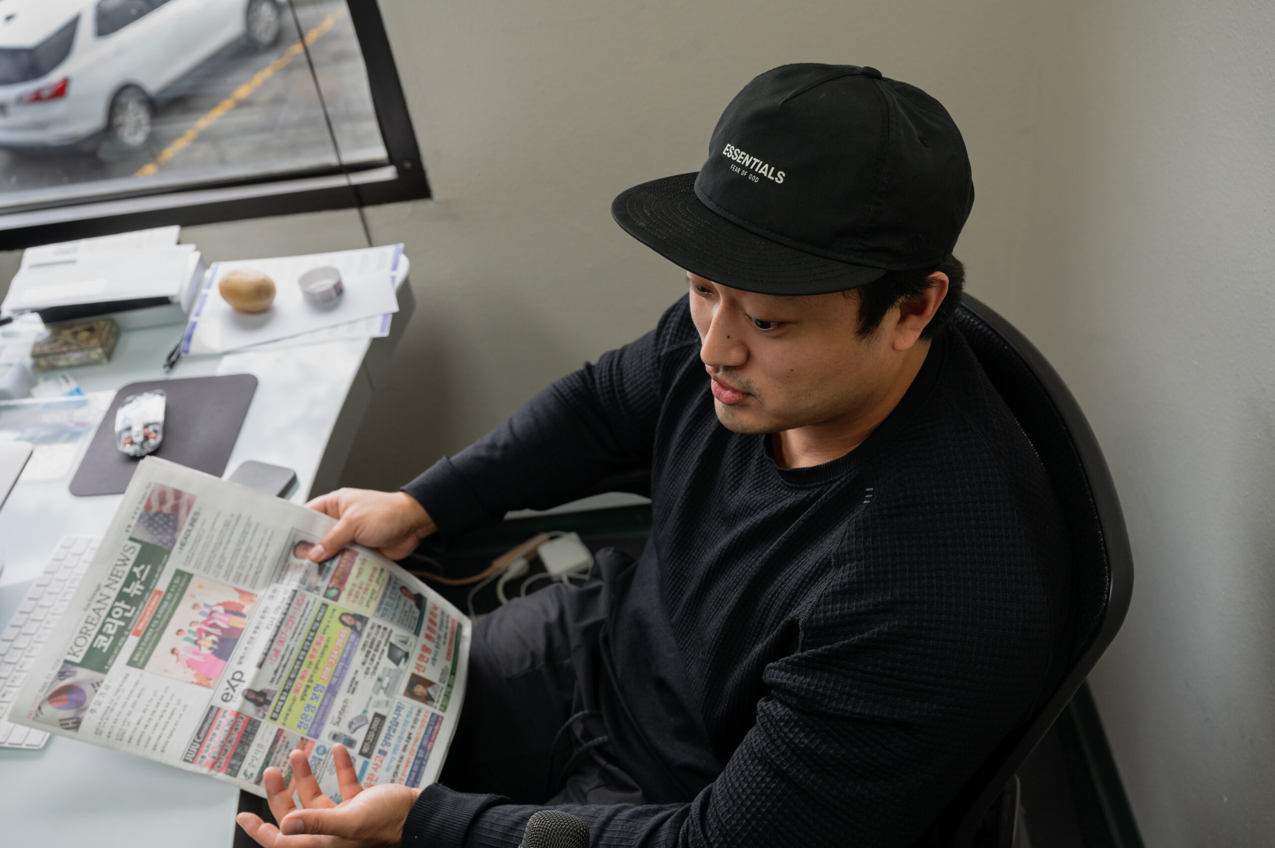 A man in a black short holds a newspaper at his desk.