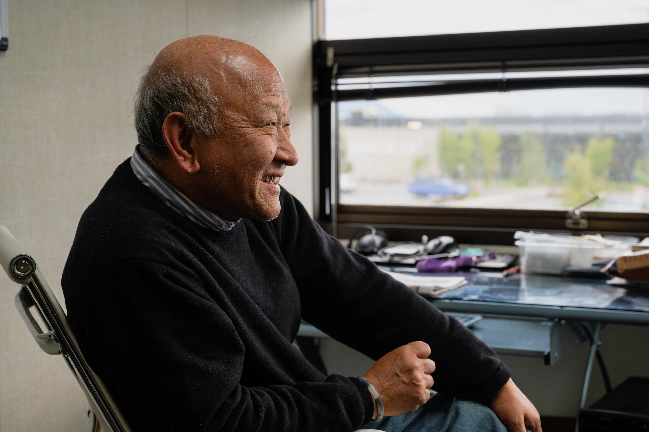 An Elderly Korean man sits astatine a desk.