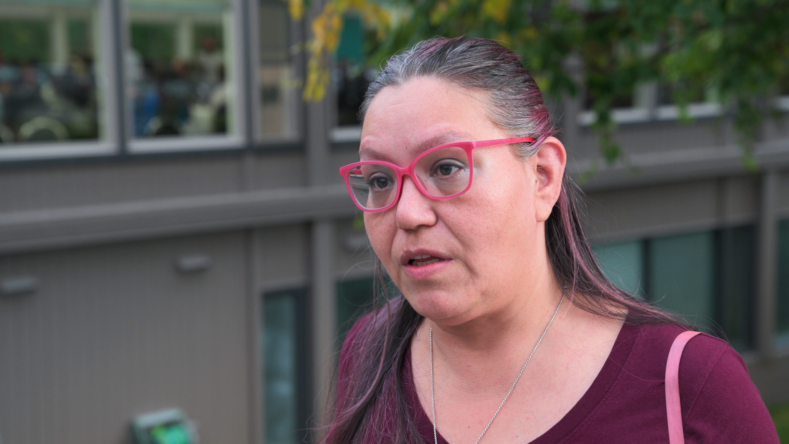 A female wearing a purple garment and pinkish glasses.